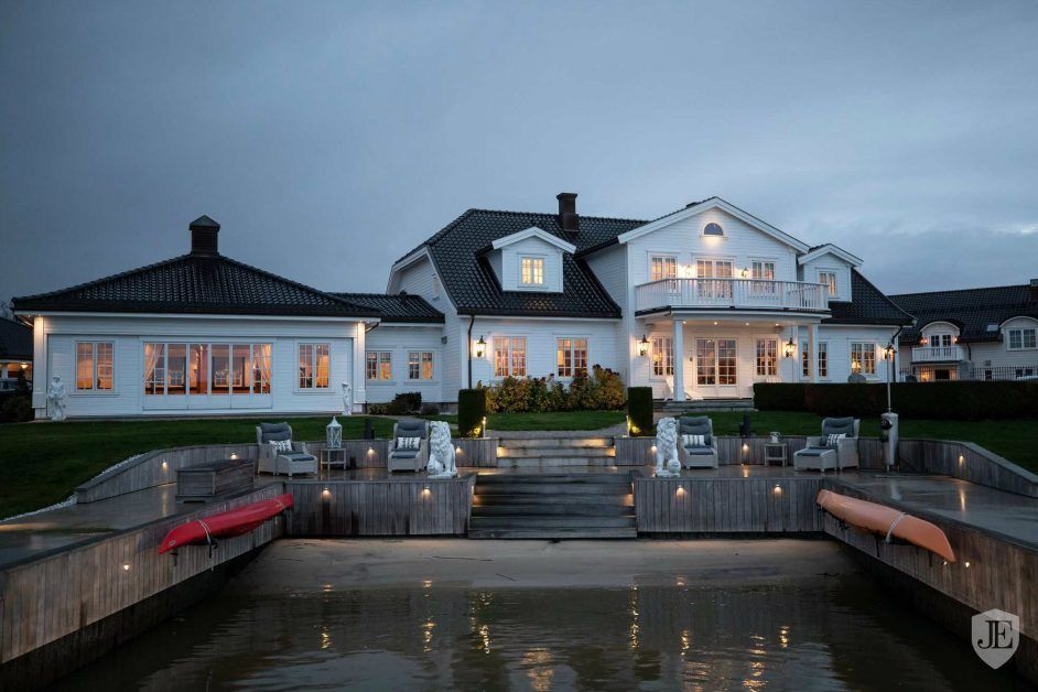 Luxury white waterfront villa illuminated at dusk with private dock